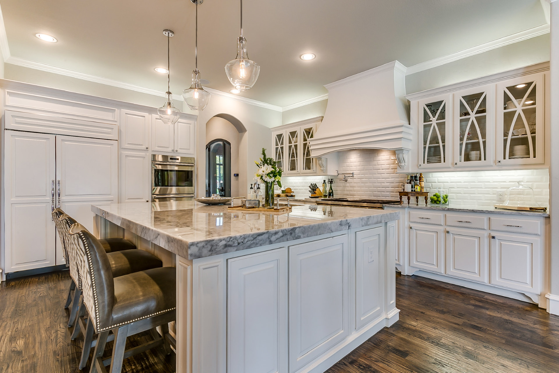 White raised-panel kitchen with a marble island and glass-front upper cabinets